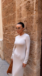 Woman in a white dress standing against a stone wall.