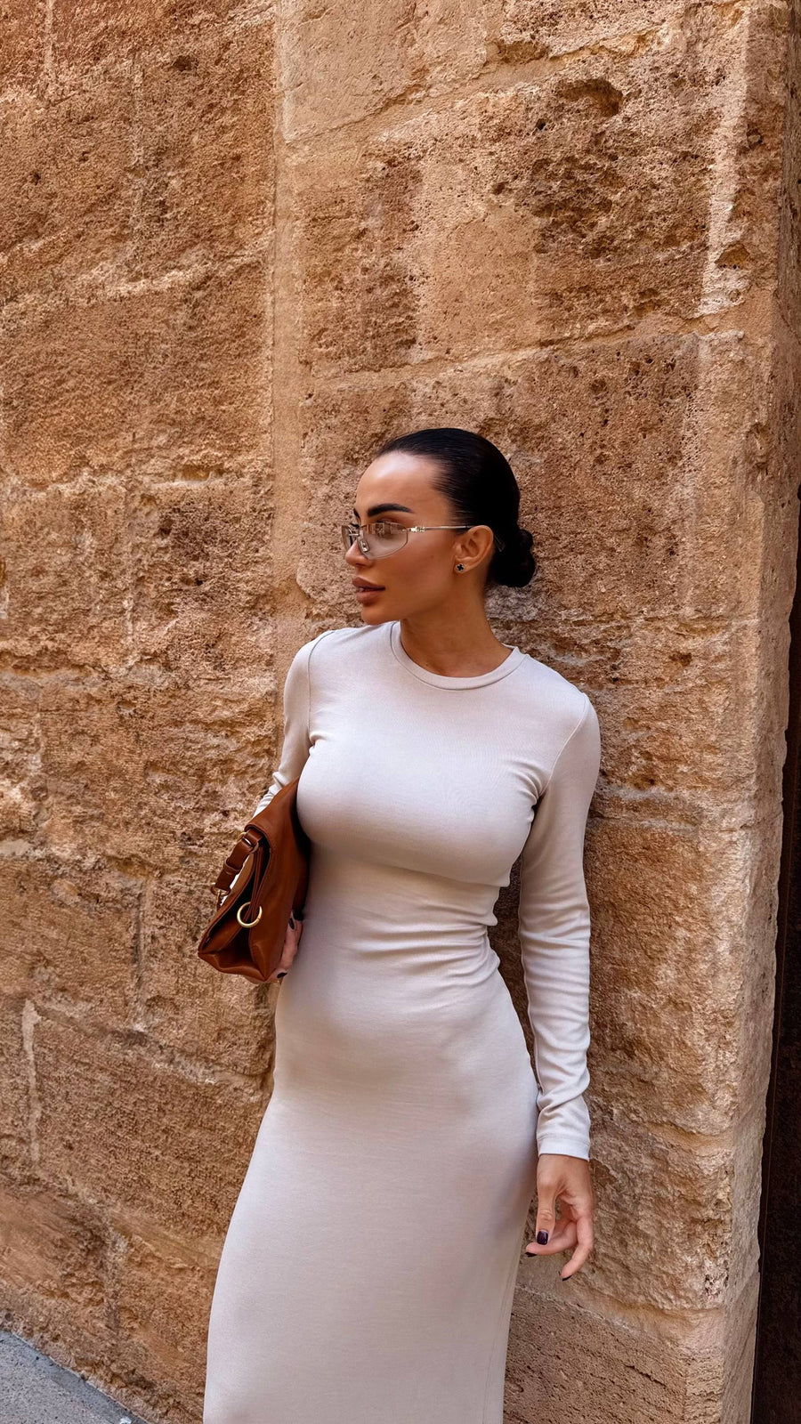 Woman in a white dress standing against a stone wall