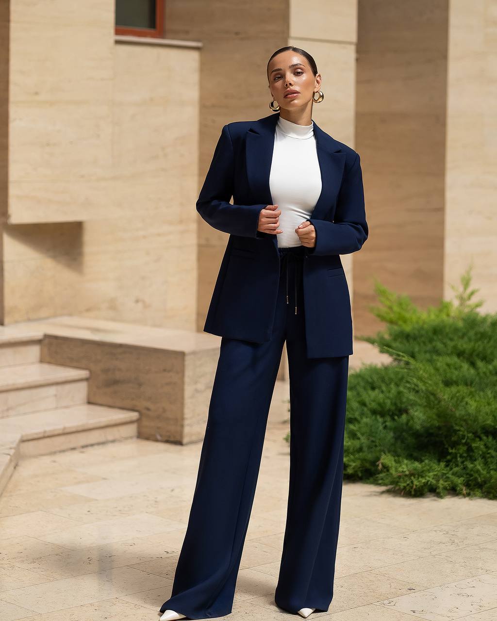 Woman in a navy suit standing outdoors with a building in the background