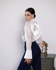 Woman wearing a white satin shirt and dark pants against a plain background