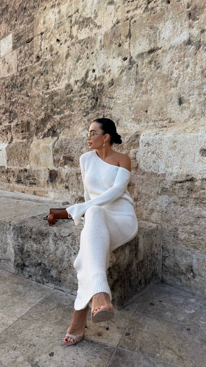 Woman in a white outfit sitting against a stone wall.