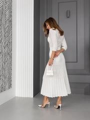 Woman in a white dress standing in a room with gray walls and a patterned wall.