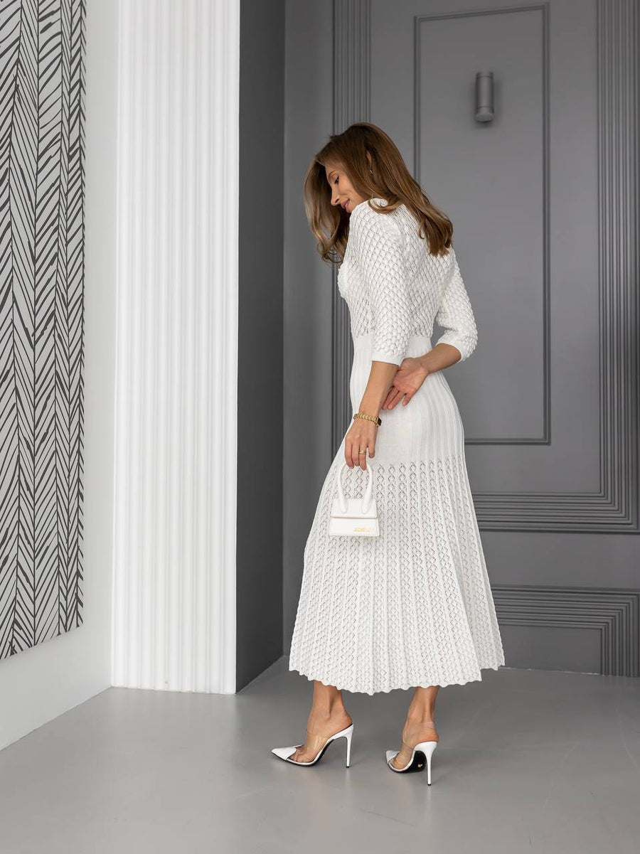 Woman in a white dress standing in a room with gray walls and a patterned wall.