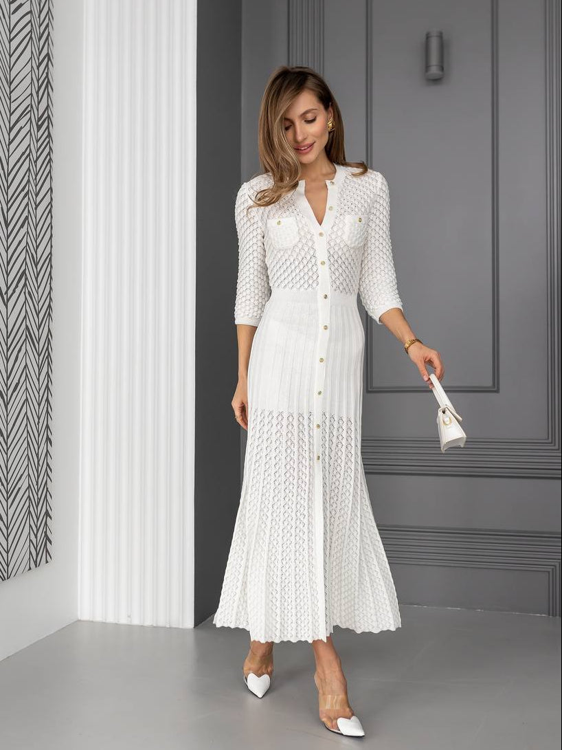 Woman in a white lace dress standing in a room with gray walls and a patterned curtain.