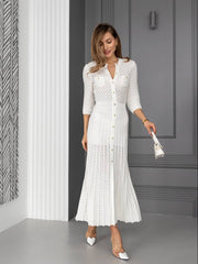 Woman in a white lace dress standing in a room with gray walls and a patterned curtain.