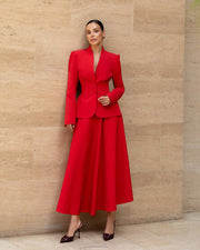 Woman wearing a red suit standing against a beige stone wall.