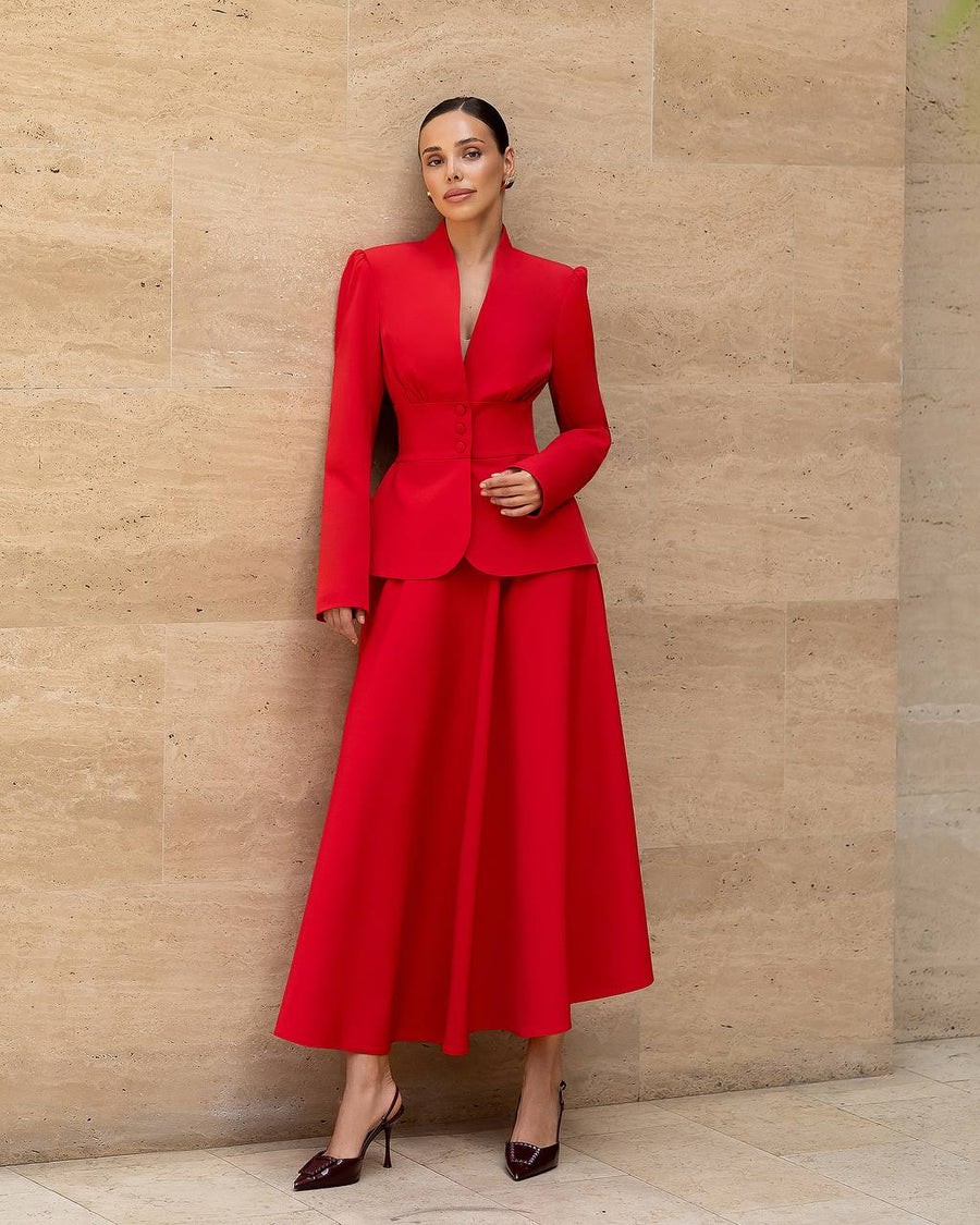Woman wearing a red suit standing against a beige stone wall.