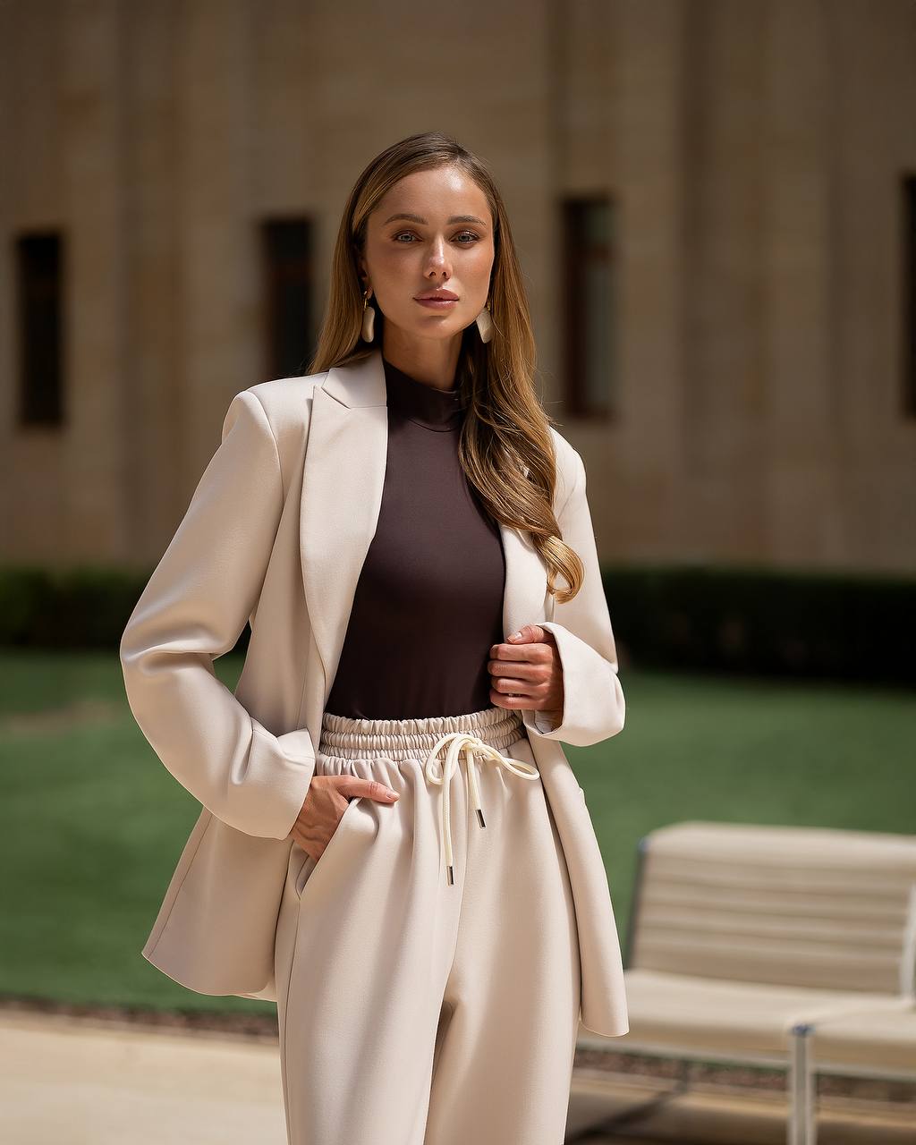 Woman in a beige suit standing outdoors with a building in the background