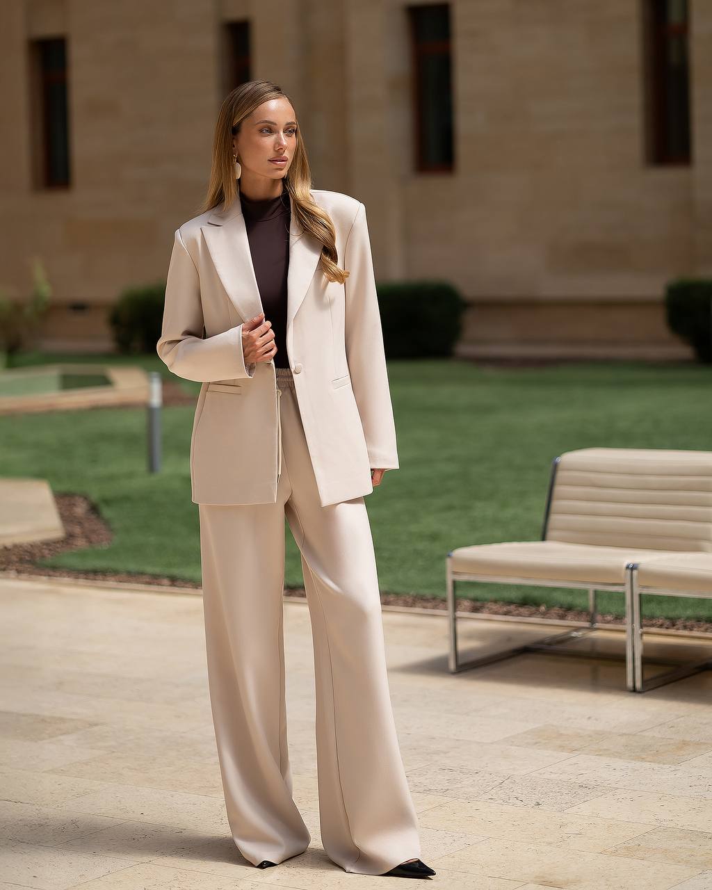 Woman in a beige suit standing outdoors on a sunny day.