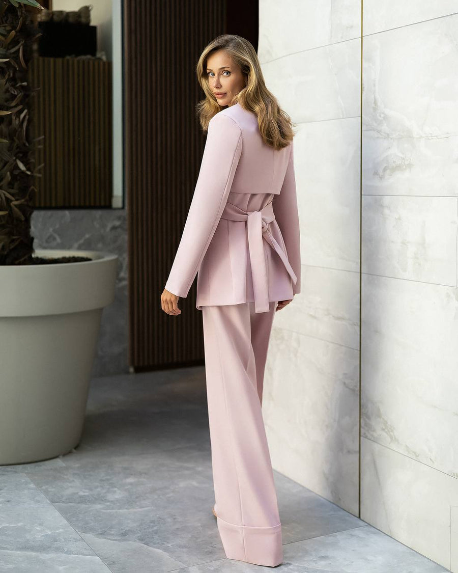 Woman in a pink suit standing in a modern indoor setting with a plant and light-colored wall.