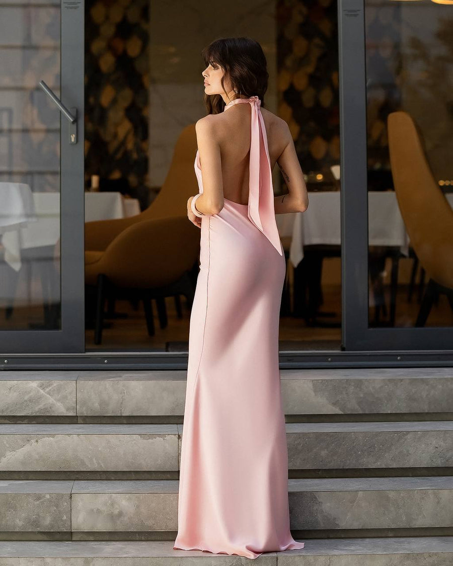 Woman in a pink evening gown standing on steps outside a building with glass doors.