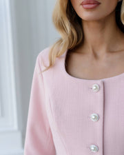 Close-up of a pink cardigan with pearl buttons on a neutral background