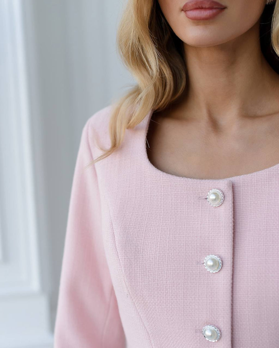 Close-up of a pink cardigan with pearl buttons on a neutral background