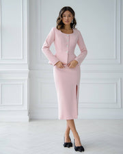 Woman wearing a pink dress suit against a white paneled wall.