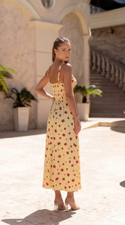 Woman in a yellow dress with red patterns standing in front of a building with columns.