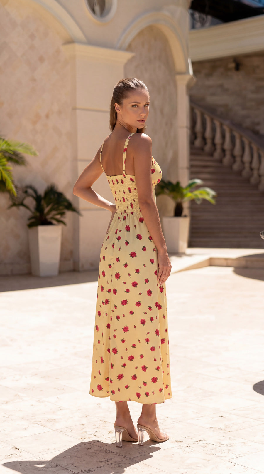 Woman in a yellow dress with red patterns standing in front of a building with columns.