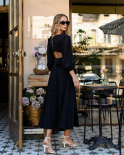 Woman in a black dress standing in an outdoor cafe setting