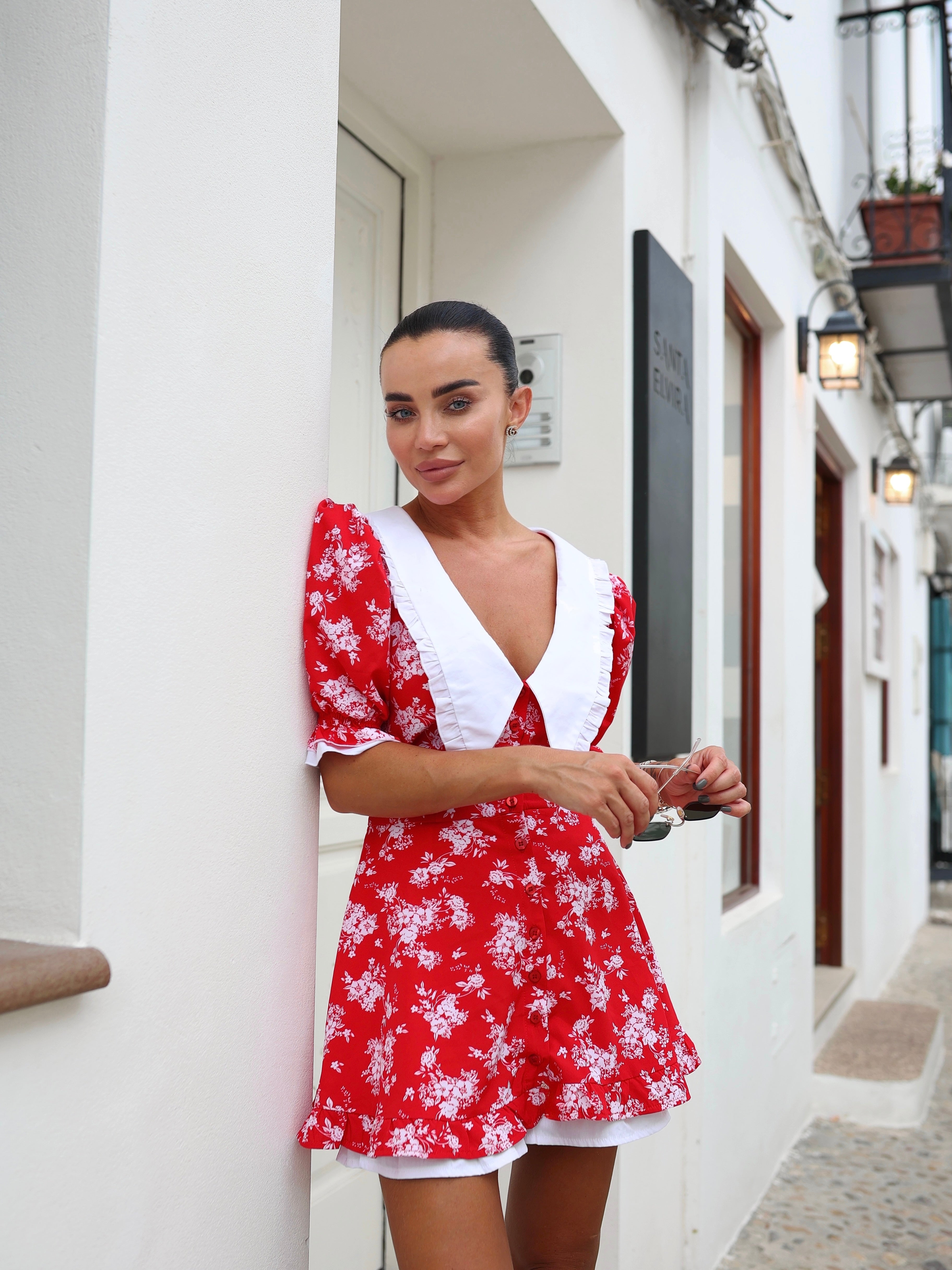 Woman wearing a red floral dress with white accents standing on a street.