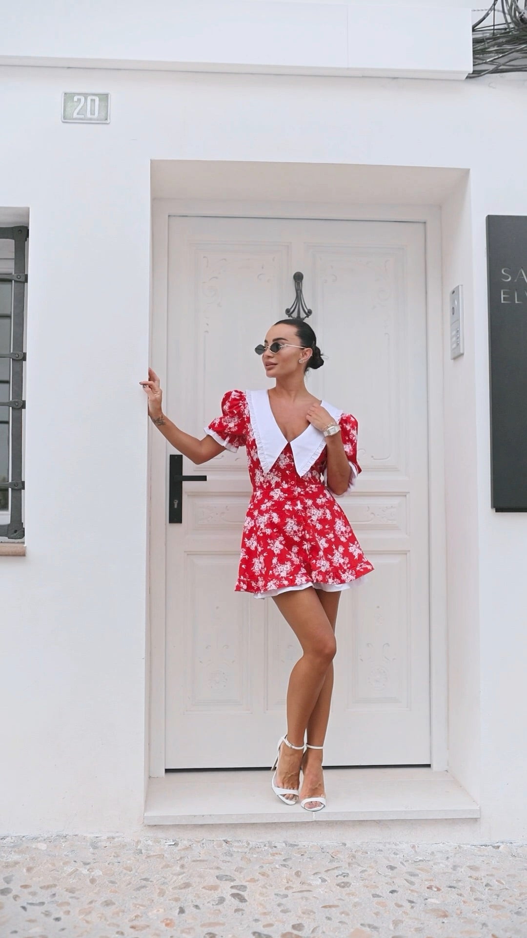 Woman in a red floral dress standing in front of a white door.