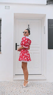 Woman in a red floral dress standing in front of a white door.