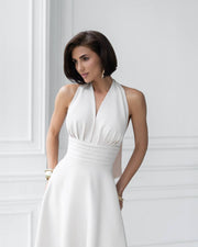 Woman wearing a white halter neck dress against a light gray wall.