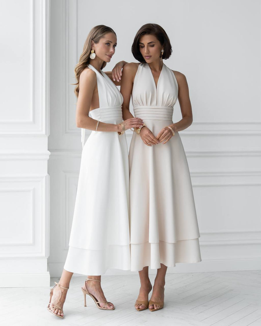 Two women wearing white halter neck dresses in a minimalistic setting.
