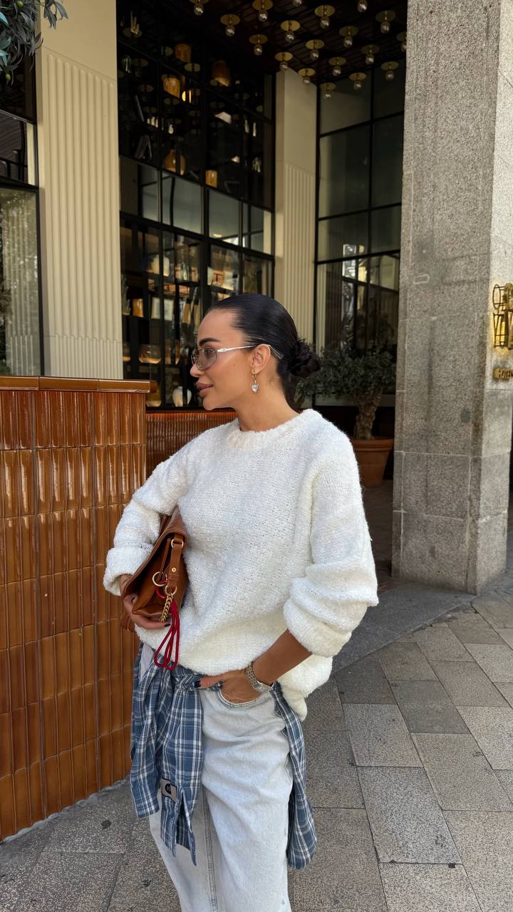 Woman in a white sweater and plaid shirt standing outside a building.
