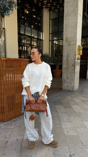 Woman in a white outfit with a brown bag walking on a sidewalk.