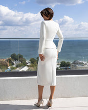 Woman in a white outfit standing on a balcony with a scenic view of the ocean.
