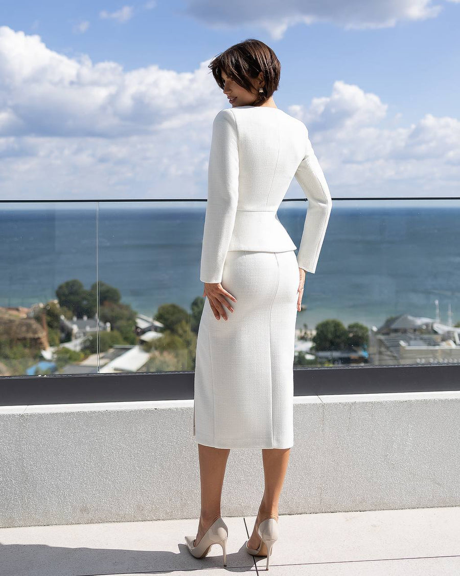 Woman in a white outfit standing on a balcony with a scenic view of the ocean.