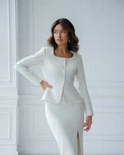 Woman wearing a white suit with a jacket and skirt against a white wall.