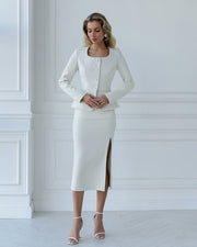 Woman wearing a white outfit with a jacket and skirt against a white wall.