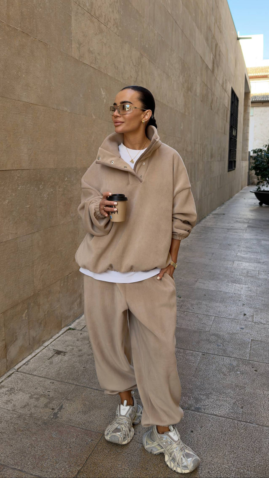 Person wearing a beige outfit with clear shoes, standing on a sidewalk.
