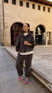 Woman in dark tracksuit with pink shoes standing in front of a stone building.