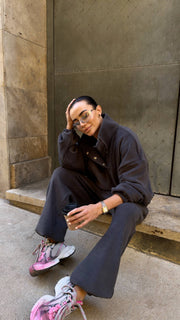 Person wearing a dark outfit with pink shoes sitting on steps.