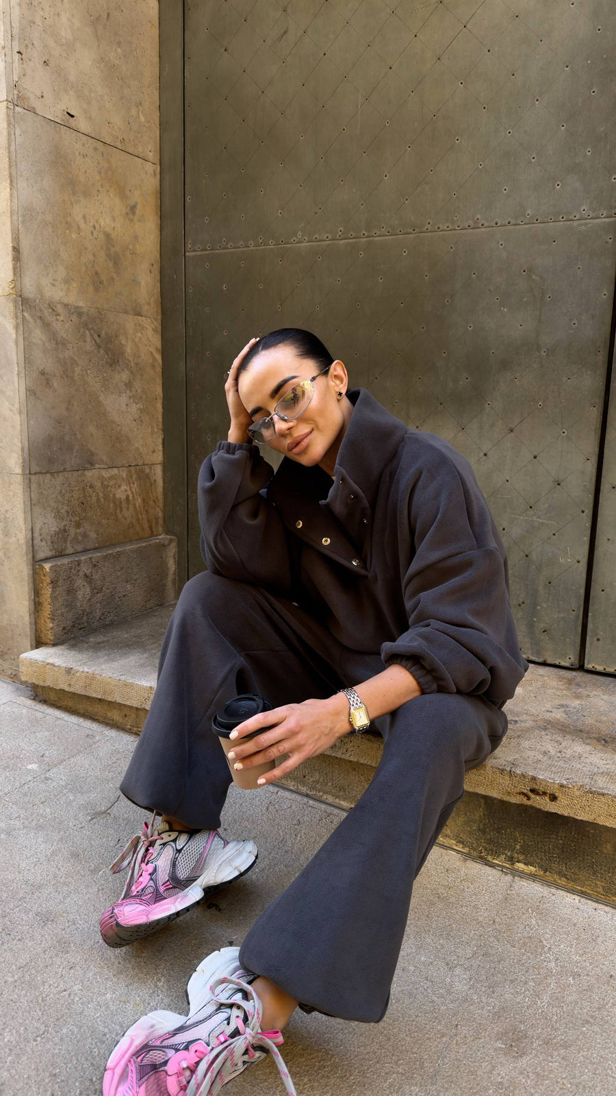 Person wearing a dark outfit with pink shoes sitting on steps.
