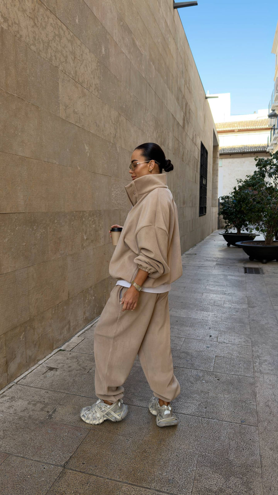 Person wearing a beige outfit standing on a sidewalk next to a building.