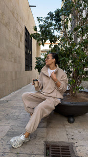 Woman in beige outfit sitting on a city street corner with a coffee cup and tissue.