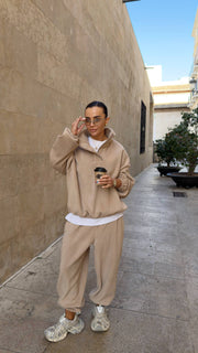 Person wearing a beige tracksuit holding a coffee cup on a sidewalk.
