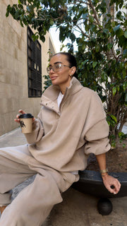 Person in beige outfit holding a coffee cup outdoors