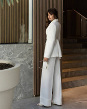 Woman in a white suit standing in a modern indoor setting with marble walls and wooden elements.