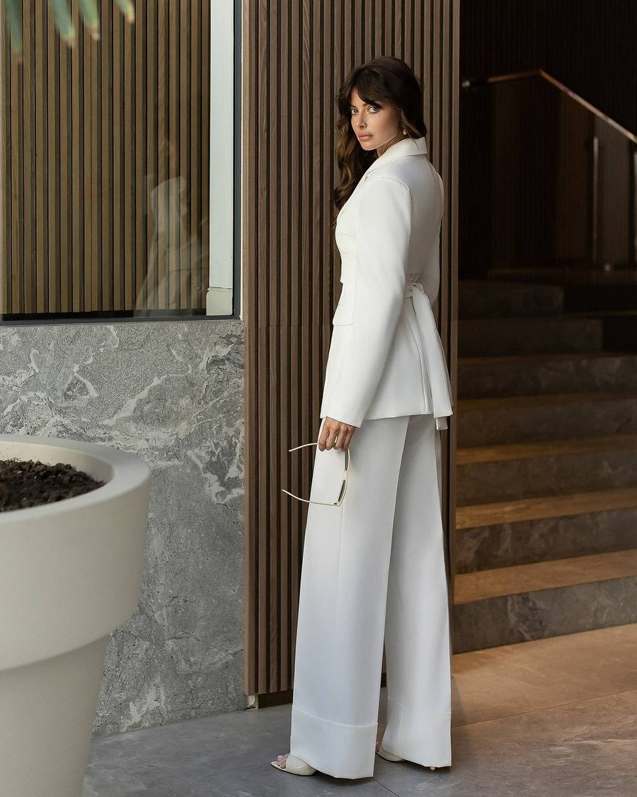 Woman in a white suit standing in a modern indoor setting with marble walls and wooden elements.
