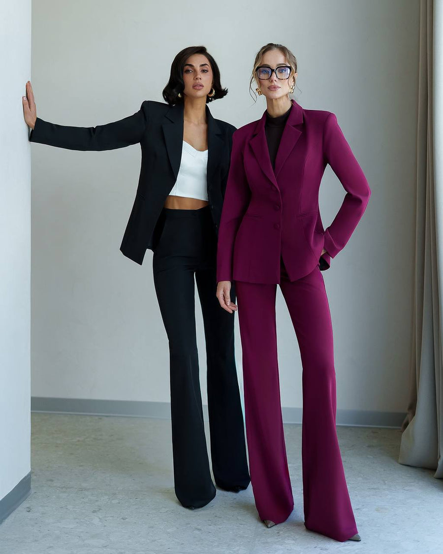 Two women in stylish suits standing against a plain background