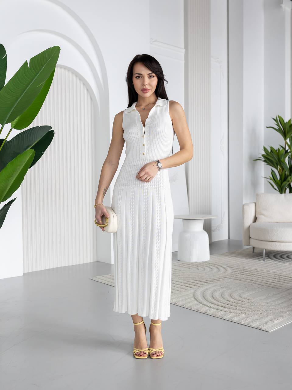 Woman in a white dress standing in a modern, minimalistic room with plants.