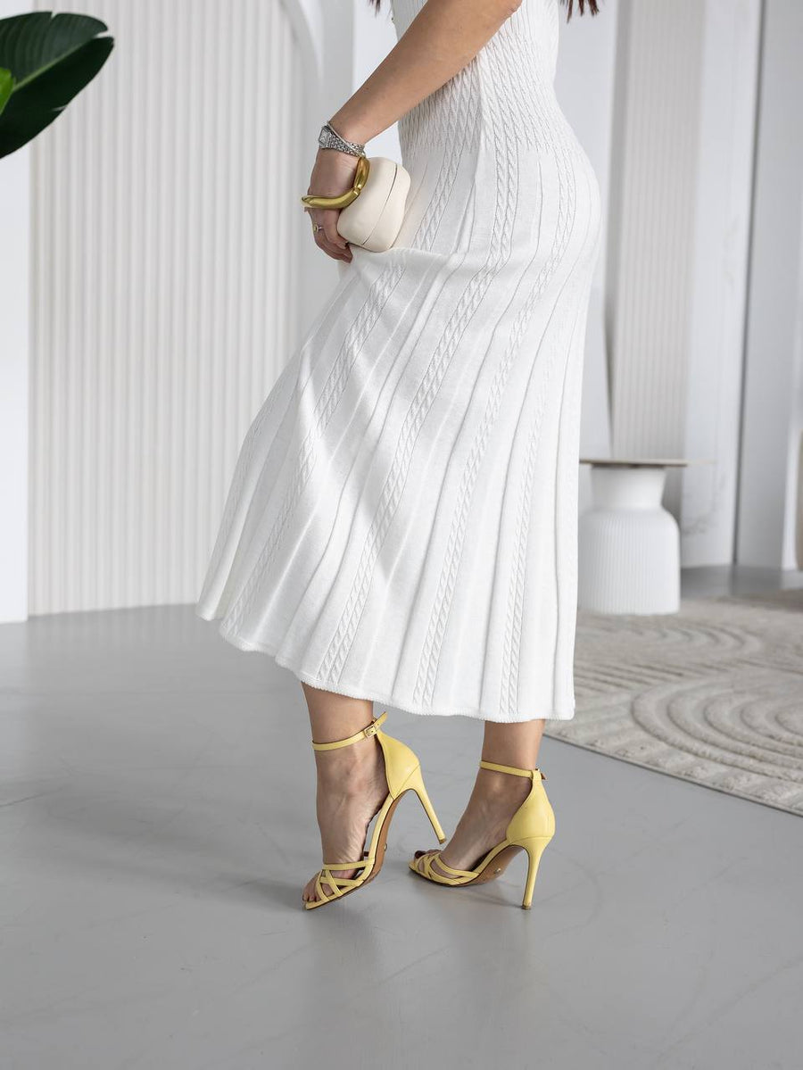 Person wearing a white dress and yellow high-heeled shoes in a minimalistic setting.