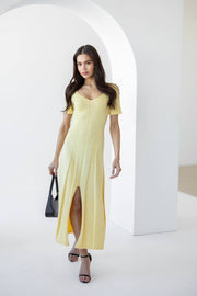 Woman wearing a light yellow dress with a black handbag in a minimalistic setting