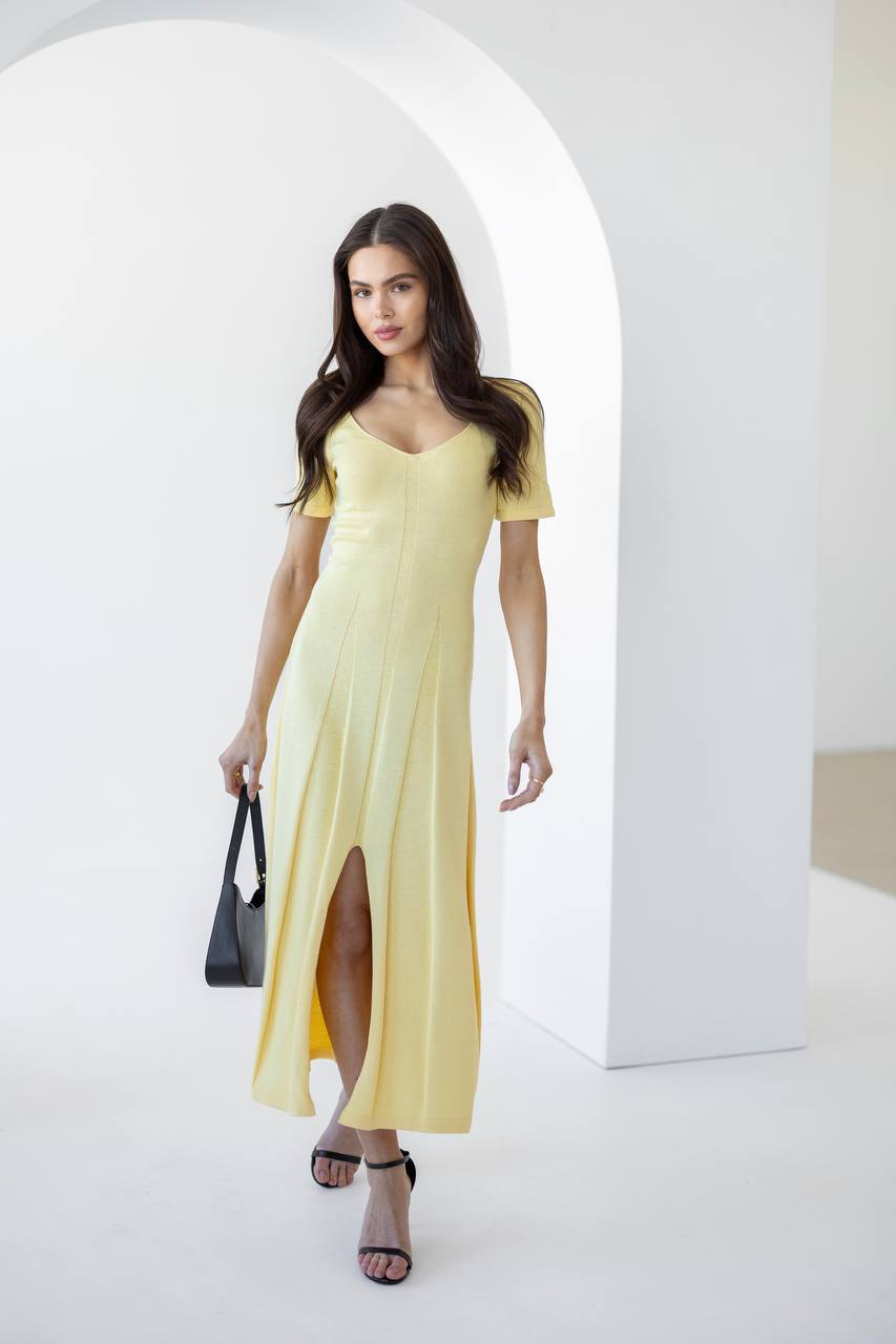 Woman wearing a light yellow dress with a black handbag in a minimalistic setting