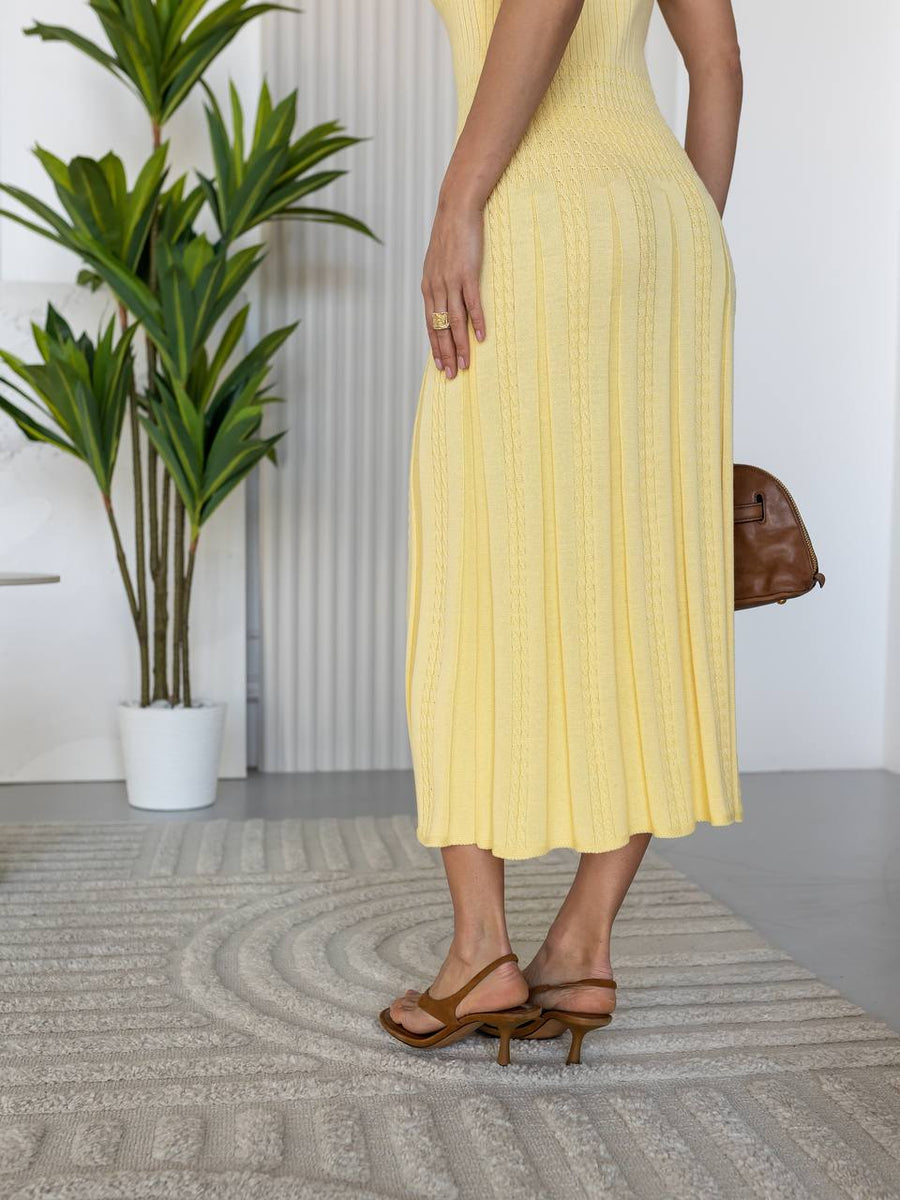 Woman in a yellow dress standing in a room with plants and a rug.