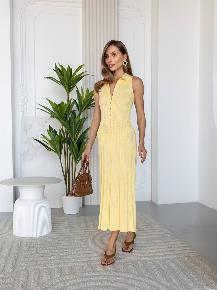 Woman in a yellow dress standing in a modern indoor setting with a plant and table.