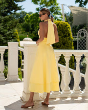 Woman in a yellow dress standing on a balcony with greenery in the background